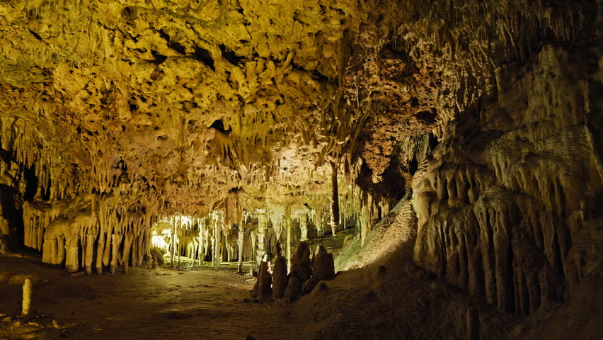 Underground cave with distinct rocky formations of stalactites and stalagmites. A colourful natural scenery in a cave with ancient cavities formed of carbonate limestone rocks in Mallorca, Spain. Royalty-Free Stock Footage #1108859031