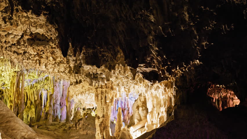 Underground cave with distinct rocky formations of stalactites and stalagmites. A colourful natural scenery in a cave with ancient cavities formed of carbonate limestone rocks in Mallorca, Spain. Royalty-Free Stock Footage #1108859035