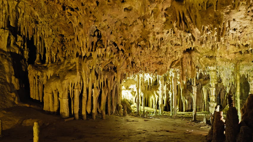 Underground cave with distinct rocky formations of stalactites and stalagmites. A colourful natural scenery in a cave with ancient cavities formed of carbonate limestone rocks in Mallorca, Spain. Royalty-Free Stock Footage #1108859039