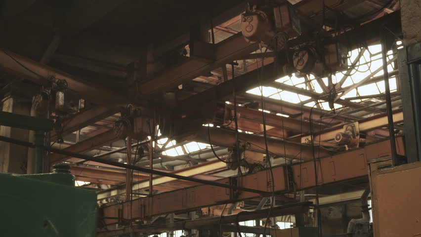 Ceiling of factory workshop with metal structures, hoists and skylights. Production building of old atmospheric metalworking plant during break in work on sunny day. Metal profiles and structures. Royalty-Free Stock Footage #1108859443