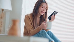 Relaxed young asian woman using mobile smartphone and drinking coffee from a mug while sitting by the window at home, The concept of balance and tranquility. - Powered by Shutterstock - Get 15% off with code: PIKWIZARD15