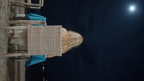 A Blonde girl sitting on a chair, by the ocean on the shore, at night. Full moon over the ocean at night. The beautiful view with Moonlight. Vertical video