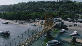 Aerial view of the yellow bridge which connect between Nusa Ceningan and Nusa Lembongan with boats anchored along the shore. Travel destination close to Bali island, Indonesia. 4K drone footage video