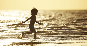 Silhouette of boy 5-7 years old running along beach. Slow motion. Concept beach holiday for young children. Happy carefree childhood. Bare feet of child on beach. Golden sunset on beach