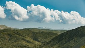Cloudy sky over mountains timelapse. Cumulus clouds swirl and roll across blue sky above green hills of mountains. Cinematic video for background. Atmosphere of amazing nature. Travel in happiness.
