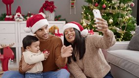 Couple and son having video call sitting on floor by christmas tree at home
