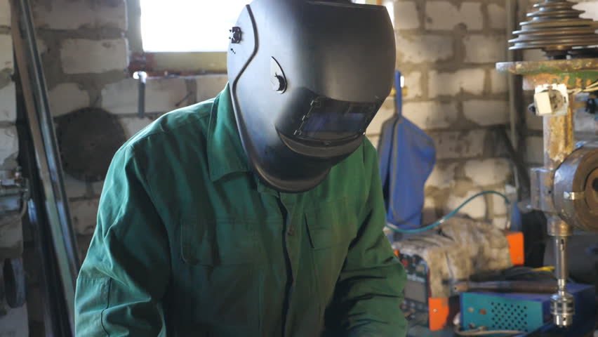 Welder finishes work and takes off his mask for rest. Happy man with beard working in his garage or workshop. Handsome guy with beard smiling during working process. Slow motion Close up Royalty-Free Stock Footage #1108874197