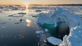 Small yacht sails between icebergs in the rays of sunset. Ship passes near huge ice cave in iceberg in Ilulissat, Greenland. Traveling on a yacht in the Arctic Circle, aerial shot - Powered by Shutterstock - Get 15% off with code: PIKWIZARD15
