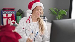 Young blonde woman doctor celebrating christmas having video call drinking champagne at clinic