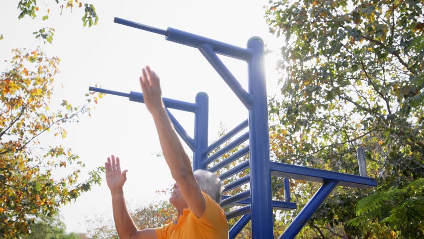 An old or elderly active Indian Asian male or Senior citizen man performing pull ups on a double bar in an open public garden gym against the morning sunlight. Concept of a Healthy lifestyle, exercise Royalty-Free Stock Footage #1108882283