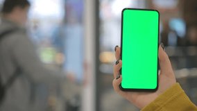 Back view of brunette holding chroma key green screen smartphone watching content. Shopping center. Shopping online. 4K