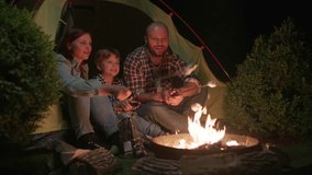Family Roasting Marshmallows over Campfire at Night. Evening camping fire. Mom, Dad and Kid camping together by the fire. - Powered by Shutterstock - Get 15% off with code: PIKWIZARD15