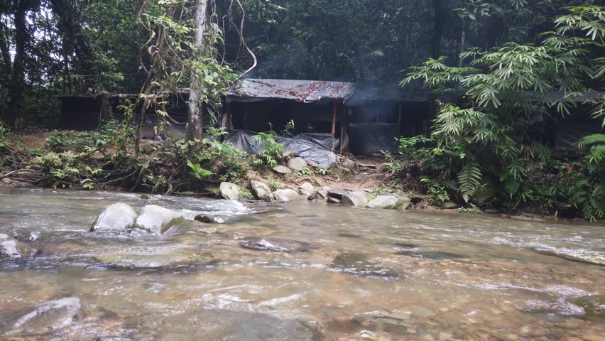 Tilting shot of a campsite in a rainforest with a small river in front. Shot on Sumatra, Indonesia