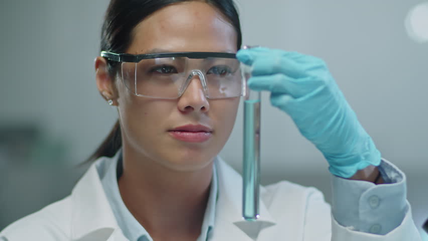 Asian female lab worker in protective eyeglasses and gloves examining blue chemical in test tube while conducting research in laboratory | Shutterstock HD Video #1108886725