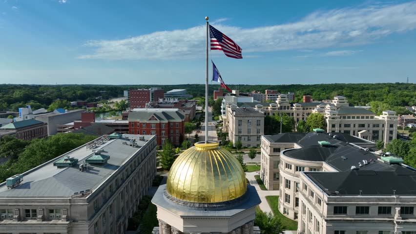 American and Iowa flags on top of the Old Iowa State Capitol Building dome in Iowa City, IA. Aerial rising shot revealing University of Iowa campus in the summer.
