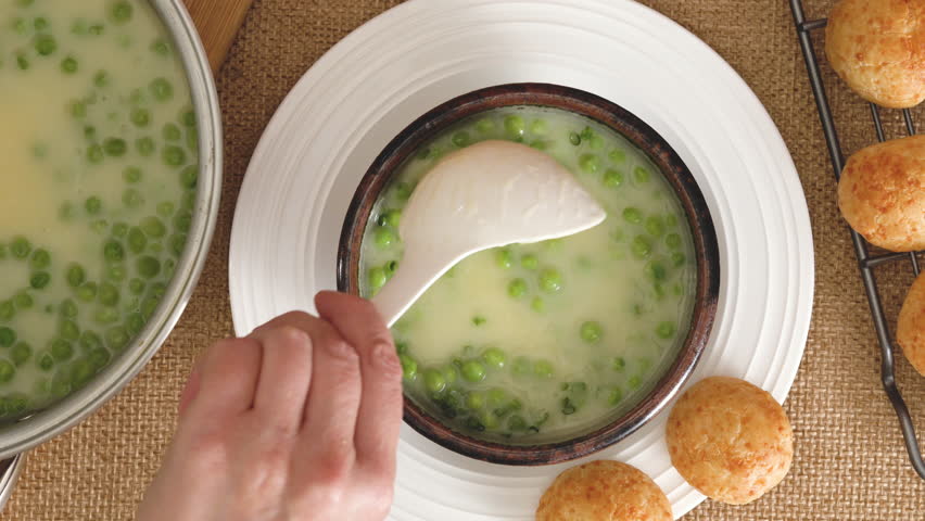 Celery cream soup with a green peas in a bowl garnished with chopped green onion and served with freshly baked cheese bread close-up on the kitchen table