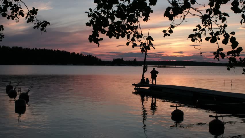 A family on a wooden pier admires the bright and beautiful sunset over the lake.