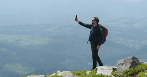 A traveler on top of a mountain is talking on the phone, taking pictures and having a video chat. Concept of communication in remote places of the world.