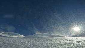 Snowflakes fly over snow drifts sparkling in rays of bright sun on a February day. Snowflakes driven by the wind knocked down into dense snowdrifts, covering the ground with a dense snow blanket