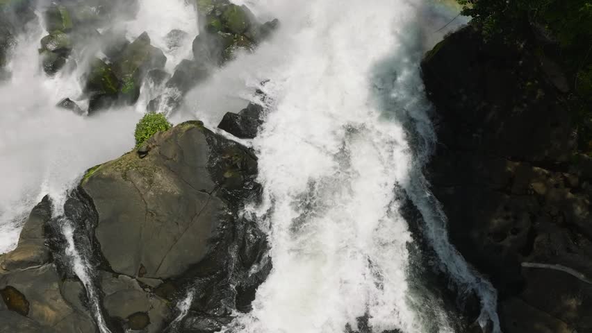 A rainbow over the stream of waterfalls from high rocks, splitting into streams, creating mist. Limunsudan Falls. Mindanao, Philippines.