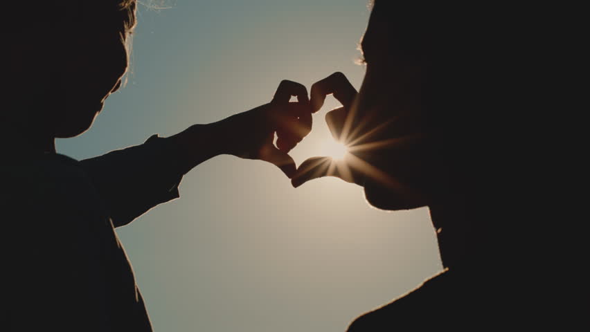 heart figure from hands, mom and daughter make a heart silhouette against the sunset background