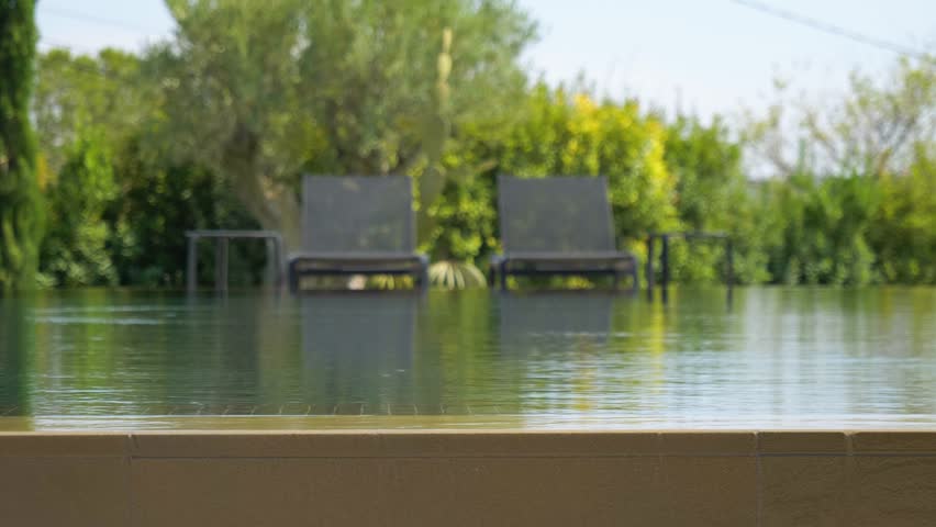 Static shot of water overflowing a pool with sun loungers out of focus