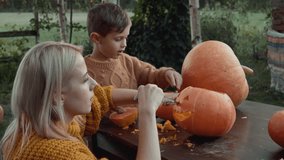 mom and son carve Halloween pumpkin on backyard table 