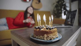 Candles burning on cake at foreground. Asian woman and her friend celebrating Happy Birthday Using Laptop Video Call. Social distancing. Girl cheers champagne glass with boyfriend online and drink