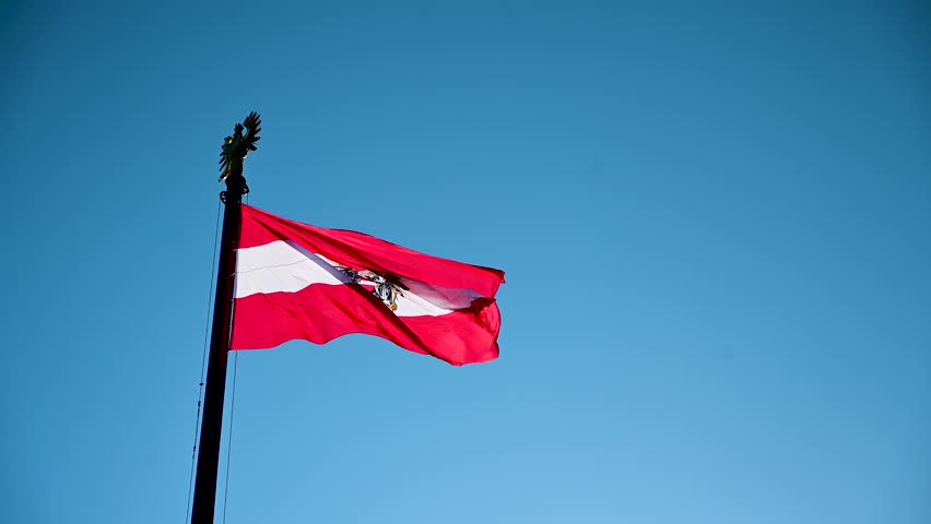Austrian flag flying on the wind. Waving national flag of Austria on flagpole against blue sky.  