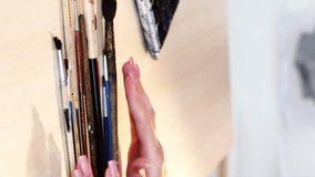 Vertical video. Art tools. Creative accessories. Closeup of woman painter hands choosing paintbrushes for drawing at artwork table studio workplace.