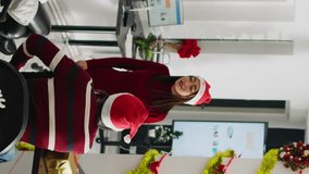 Vertical video Diverse workers wearing Santa hat enjoying Christmas spirit mood playing pretending acting game during break. Coworkers having fun doing funny gesticulations during pantomime in xmas