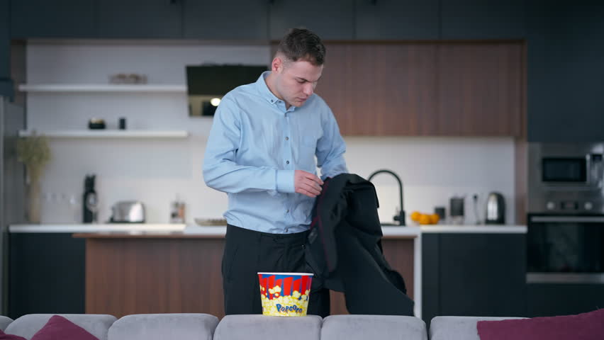Tired young man taking off elegant jacket taking popcorn looking away thinking. Portrait of fatigue Caucasian freelancer businessman at the end of week at home indoors | Shutterstock HD Video #1108911213