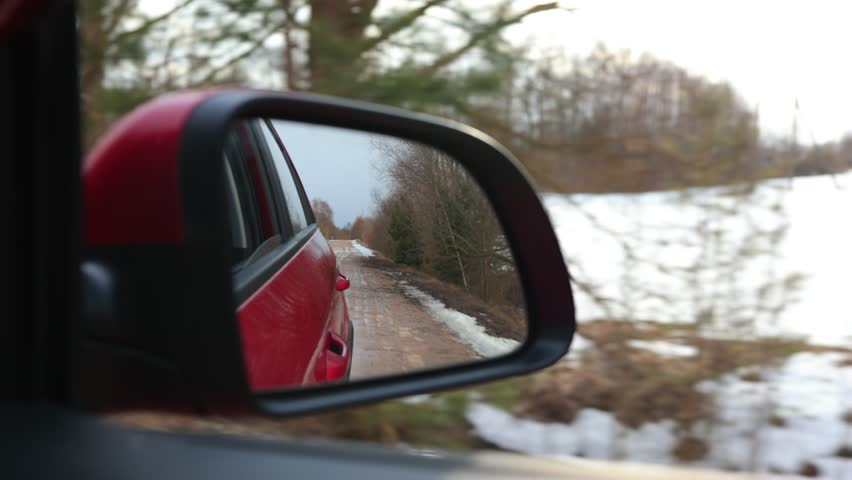 Red automobile in motion. View in the rear view side mirror of a auto, driving a red car along the track