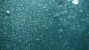 Detailed underwater slow-motion video of air bubbles and minute particles in a radiant blue setting.