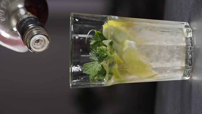 Bartender pouring liquid out of bottle to make mojito cocktail closeup. Vertical footage. Slow motion. Refreshing iced lemon mint beverage. Cool spirit filling citrus alcohol drink cup. Making tasty | Shutterstock HD Video #1108919817