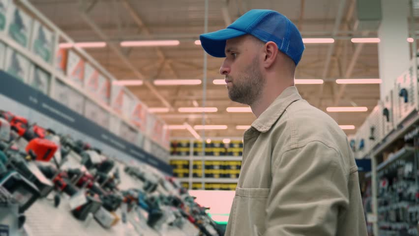 A man in a hardware store chooses a new screwdriver next to a showcase of power tools for repairs in the house.  Royalty-Free Stock Footage #1108920117