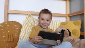 Cute little kid boy using digital tablet technology device in his bed. Small child hold computer watching movie at home. 4K
