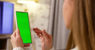 Back view of brunette holding smartphone with green screen watching content