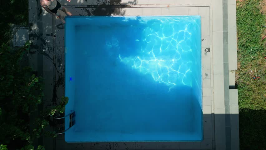 Slow motion, top view, swimming pool in a hotel, one short-haired athletic man sits on the edge of the pool, he dives into the water, swims a little below the surface and emerges, wiping his face | Shutterstock HD Video #1108924005