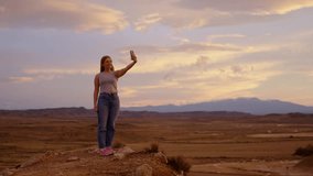 Young woman live streaming in a desert at sunset. Person having video call outdoors.