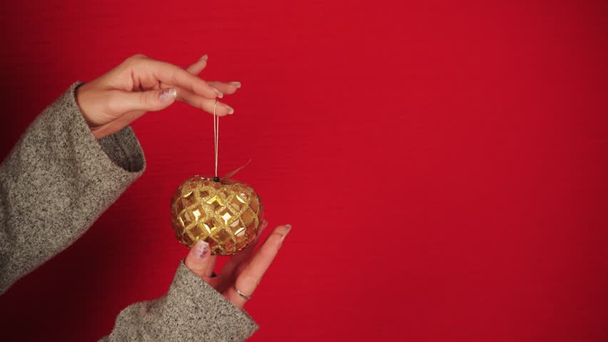 A golden Christmas ball is like a symbol of the new year and Christmas. Female hands hold a Christmas tree toy. The girl gives a festive mood. New Year symbol of the dragon. Festive atmosphere. | Shutterstock HD Video #1108925353