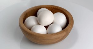 Close-up footage of a wooden bowl with eggs on a white background. Footage on a rotating table.