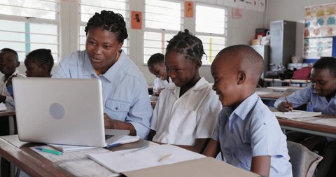 Close-up. Black African female teacher sitting and assisting African children at their desk with a task on a laptop in a classroom in Africa 库存视频