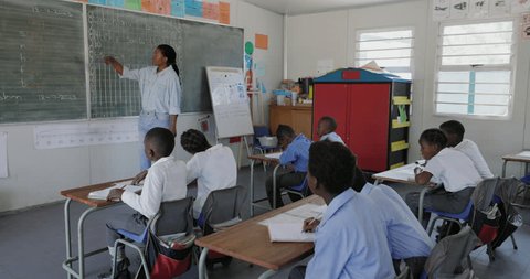 Close-up panning view. Black African female teacher standing at the chalkboard teaching children in a classroom in Africa 库存视频