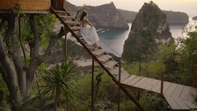 Nusa penida, Bali, indonesia, 4K video of woman white dress sit of tree house and looking at Atun beach on tree house, Nusa Penida island at sunrise. Popular travel destination on Bali, indonesia.