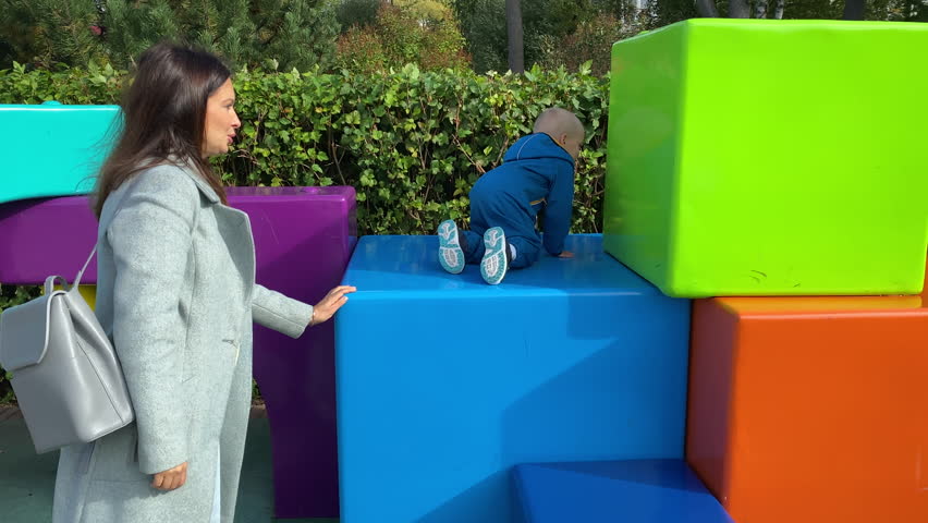 mother with toddler child in amusement park, happy little boy climbing on colorful cubes. Divo Island, St. Petersburg, Russia