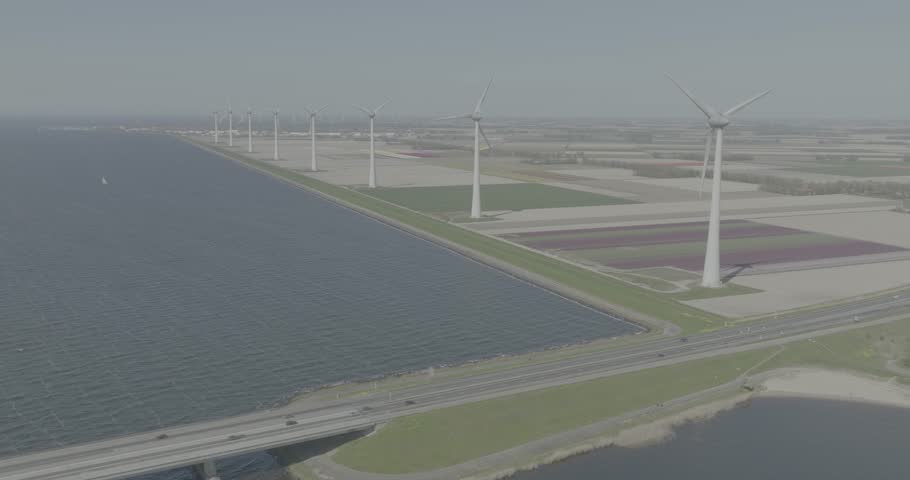 D log color profile, aerial drone view of windturbines along a shore line, next to colored tulips fields in the netherlands. Sustainable energy generation. Dutch clean energy generation
