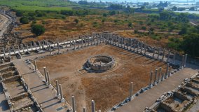 In this captivating aerial stock video, the remarkable ruins of the ancient city of Perge in conteprorary city of Antalya, Turkey are shown. The camera gracefully glides above, offering a panoramic