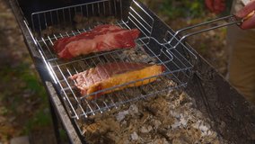 Close-up of man cooking juicy pieces of meat on grill. Stock footage. Man cooks two delicious pieces of red meat on coals. Grilling meat outdoors in summer