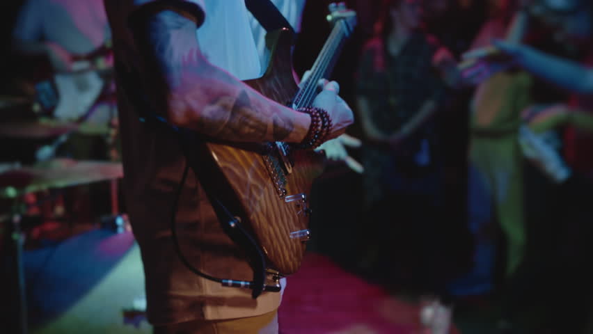 Concert rock band performing on stage with singer guitar closeup of male hands. Crowd of people listening. Music punk, heavy metal or rock group. The guitarist performs on stage. Stage light, smoke.